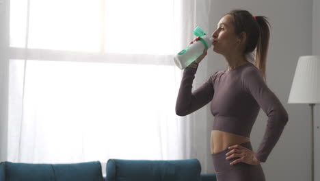 pretty-woman-with-ponytail-is-drinking-water-after-training-at-home-relaxing-and-resting-after-gymnastics-healthy-lifestyle-and-wellness